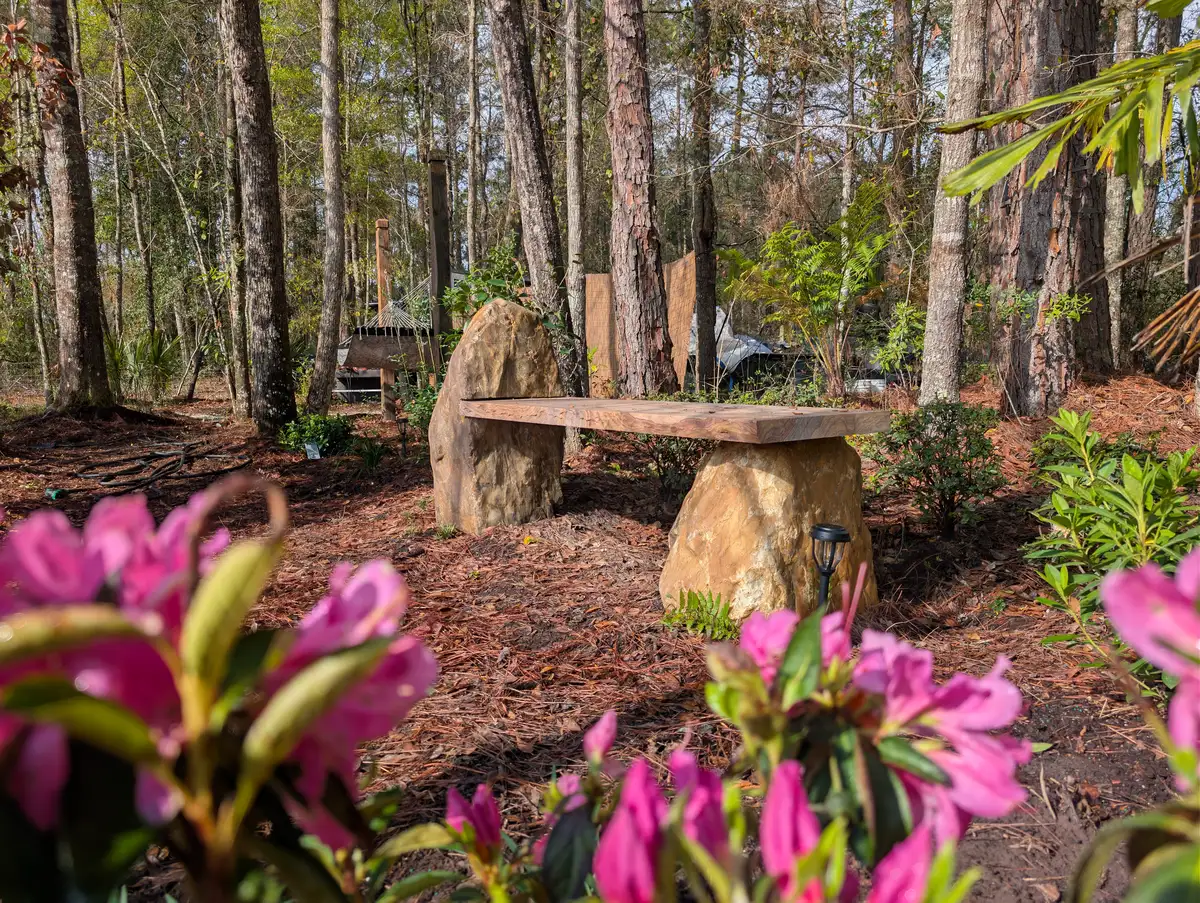 Woodland planting around stone-supported garden seating and flowering shrubs